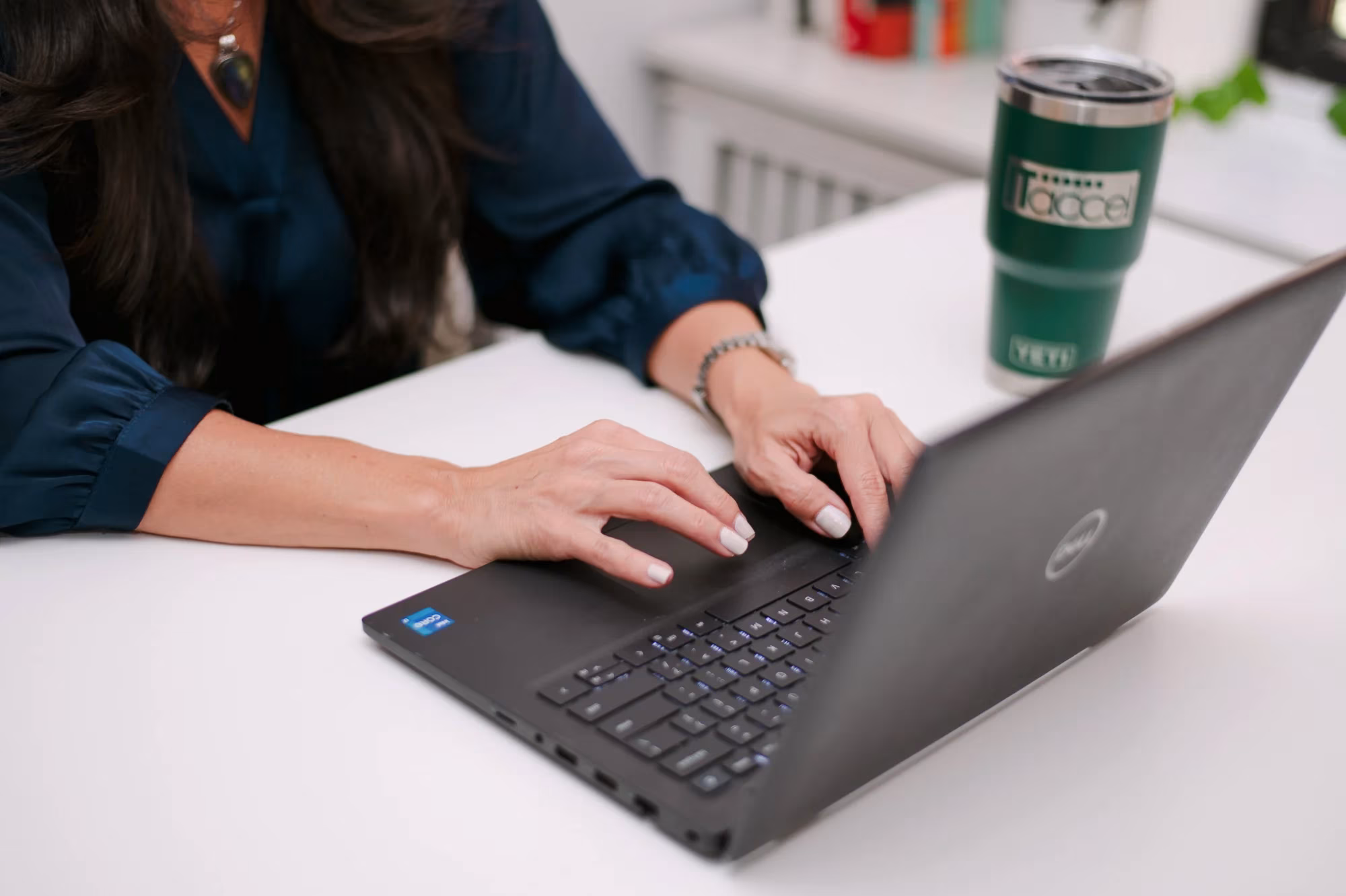 recruiter-working-at-laptop-it-accel. IT Accel recruiter typing on a laptop beside a branded tumbler at a New York office desk