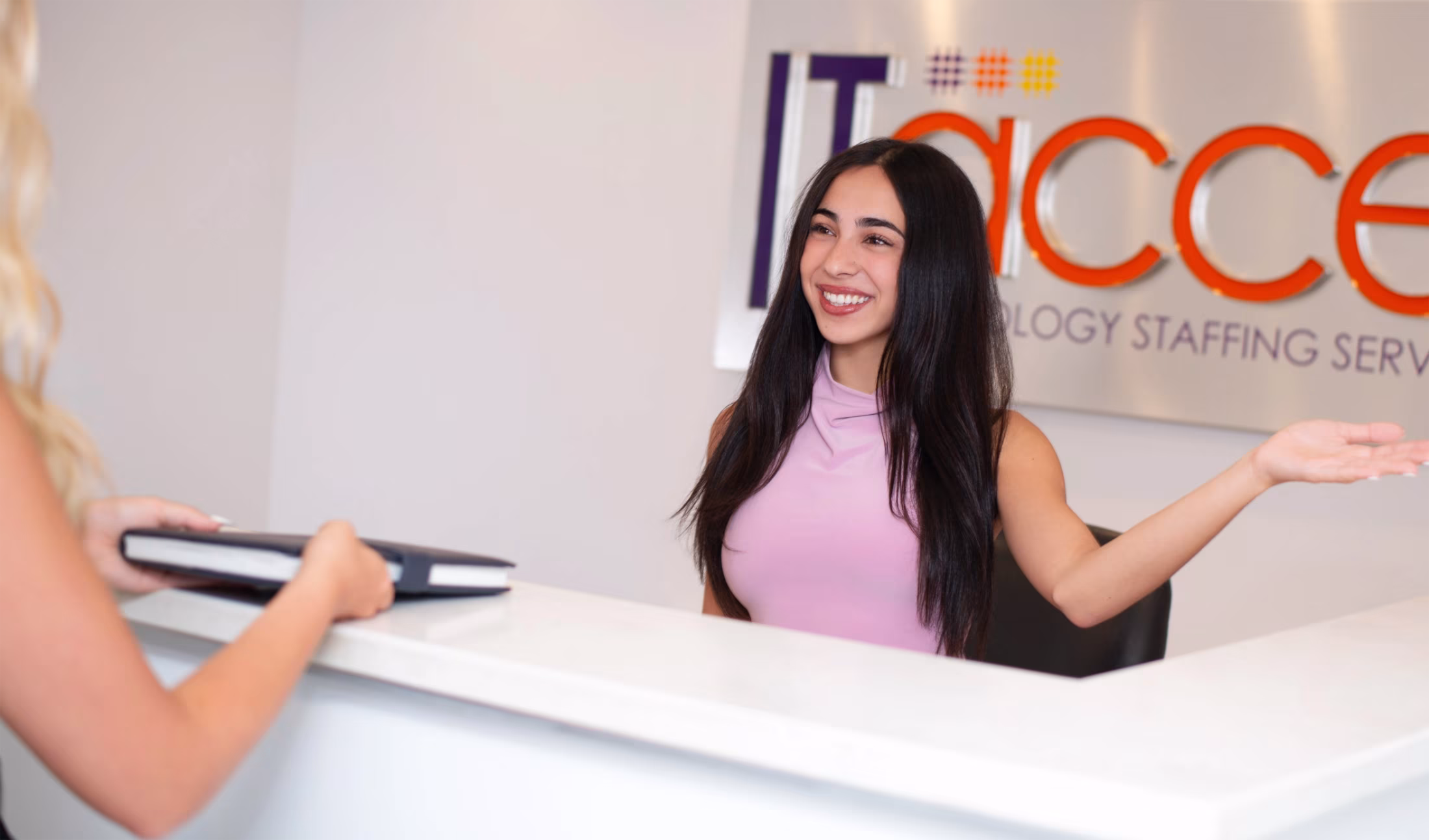 receptionist-welcoming-visitor-reception-desk-itaccel. IT Accel receptionist welcoming a visitor with an open gesture at the front desk